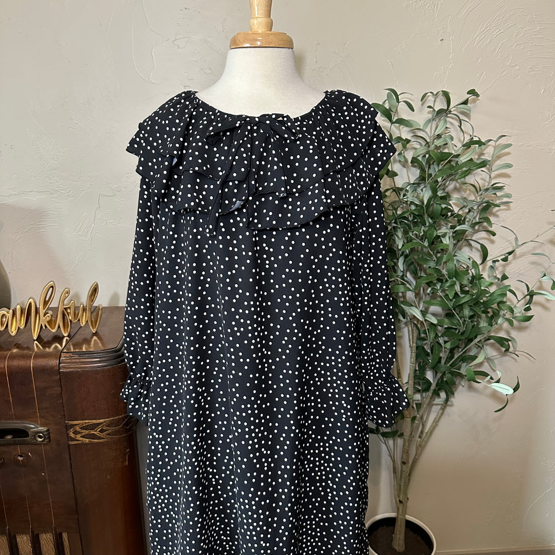 Upper front view of the round neckline, bow and ruffled sleeve cuffs