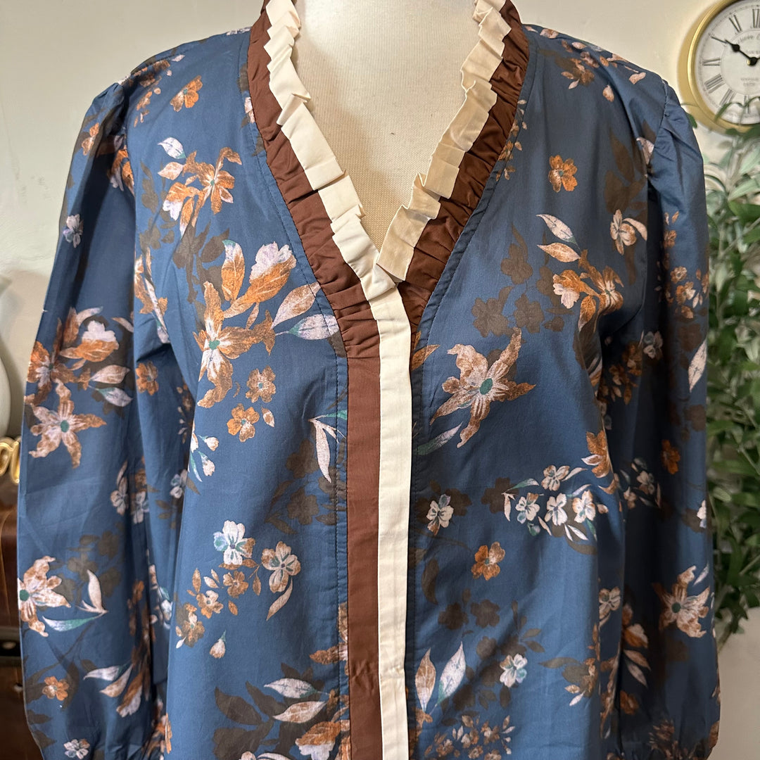 Close-up of the cream pleated ruffle and brown trim at the V-neckline