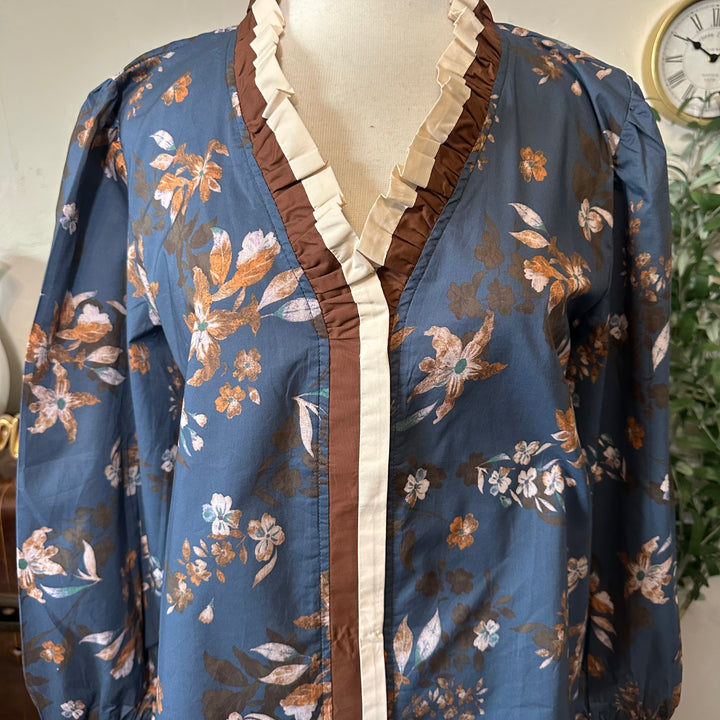 Close-up of the cream pleated ruffle and brown trim at the V-neckline