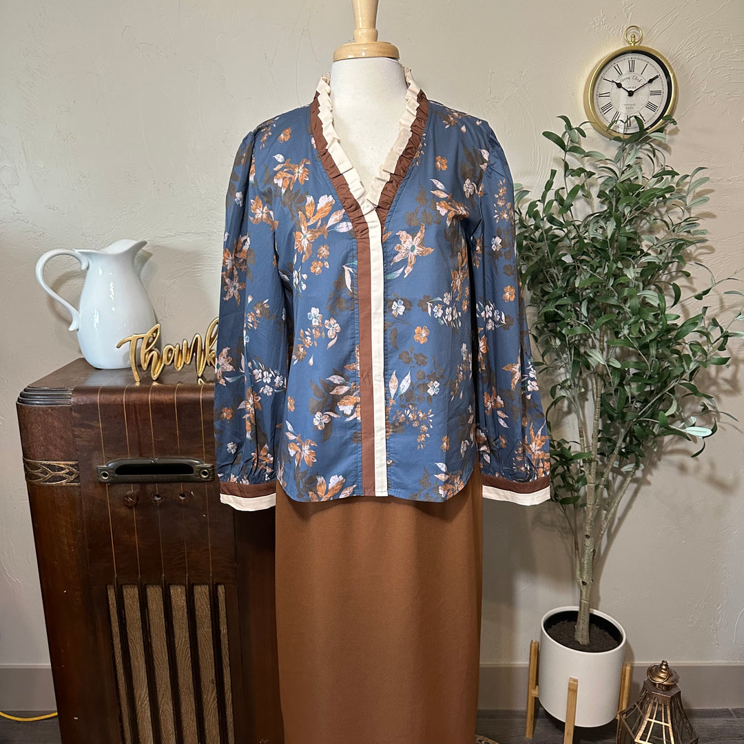 Eleanor Ruffle Collar Floral Blouse in dusty blue, front view with the pleated ruffle V-neck and brown skirt